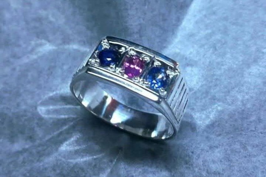 Een zilveren ring met een rechthoekige band en een centrale zetting met drie edelstenen. 2