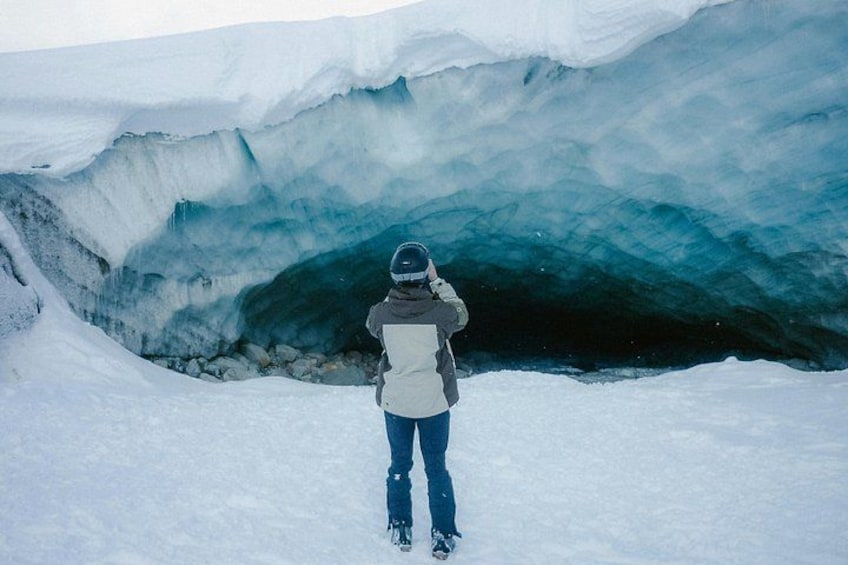 A person standing in front of a large ice cave. 5