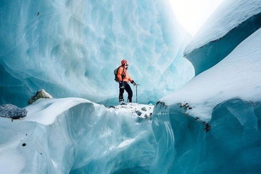 A person in a red jacket and helmet standing on a snow-covered ridge in a glacier. 3