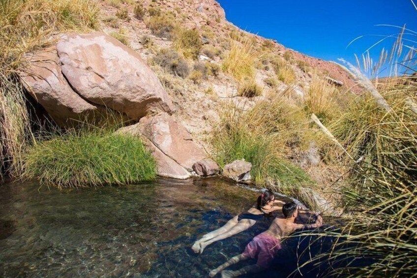 A person wading in a clear stream surrounded by rocks and grass. 3