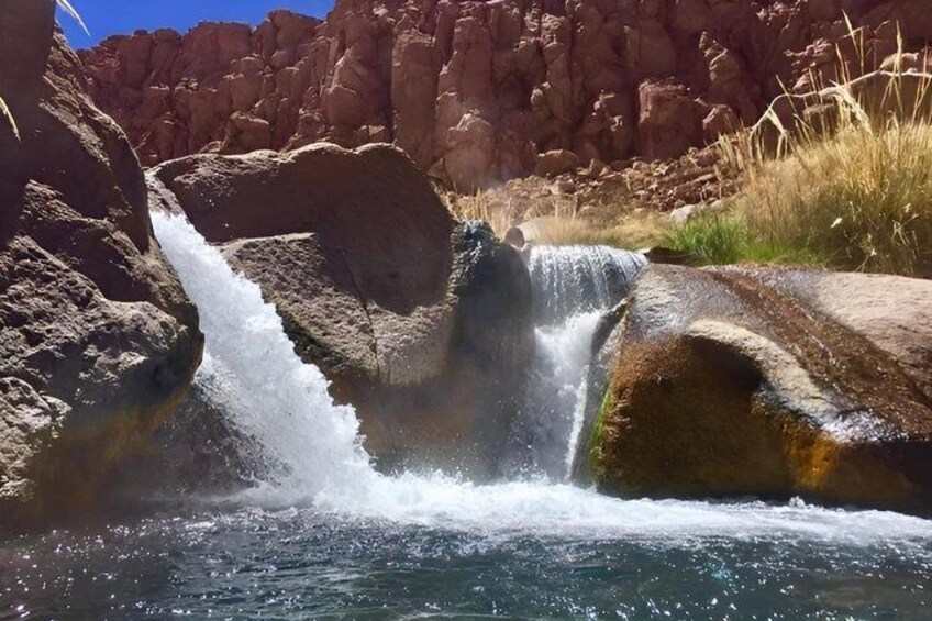 A waterfall cascading over rocks in a canyon with clear blue water. 2