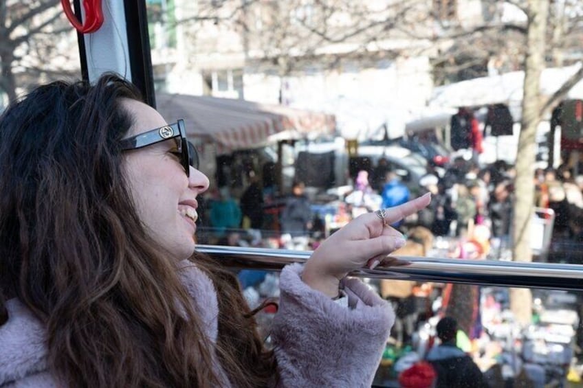 A person in a fur coat pointing out of a bus window at a crowded outdoor market. 3