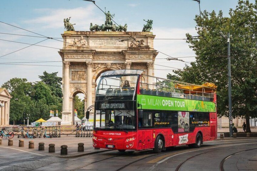 Un autobús de dos pisos rojo con la leyenda 'Milan Open Tour' en la carrocería, pasando por el Arco del Triunfo en Milán. 1