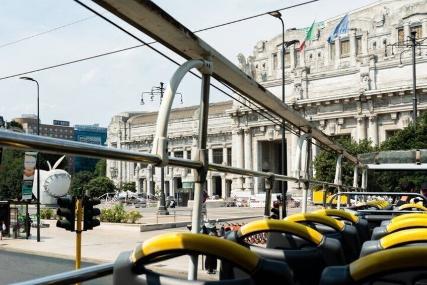 Una estación de autobuses con vehículos amarillos, un edificio grande con columnas y una calle con semáforos. 2