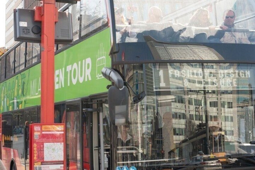 A double-decker bus with 'Milton Keynes Tour' written on the side, a red pole, and a building with a glass facade. 2