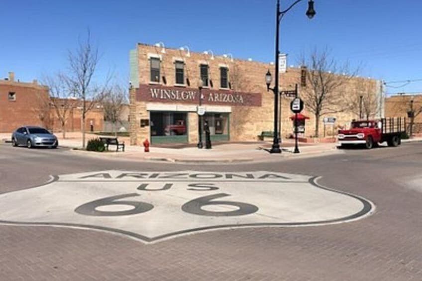 A street with a large Arizona 66 sign, a building labeled 'WINSLOW ARIZONA,' and a red truck parked on the side. 3