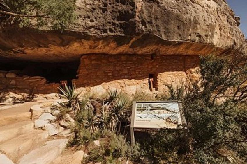 Eingang zu einer Höhle mit einem Schild, felsigem Gelände und vereinzelter Vegetation. 1