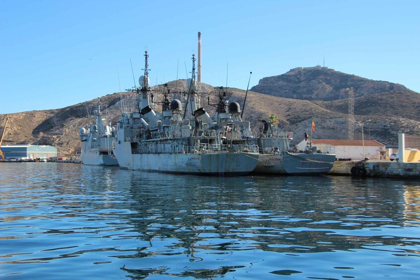 A large naval ship docked at a harbor with mountains in the background. 3