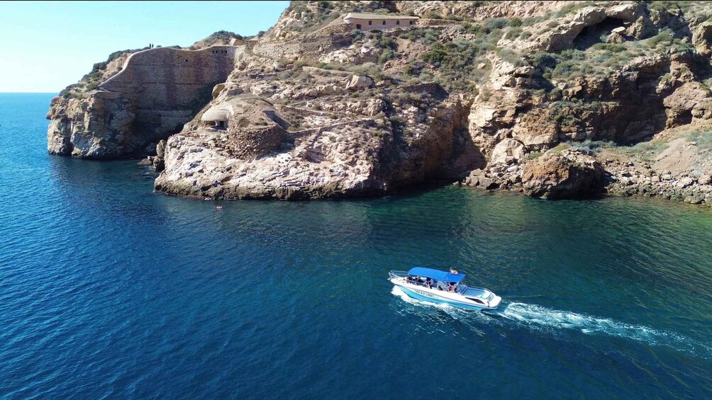 A boat on clear blue waters near rocky cliffs with a building on top. 1