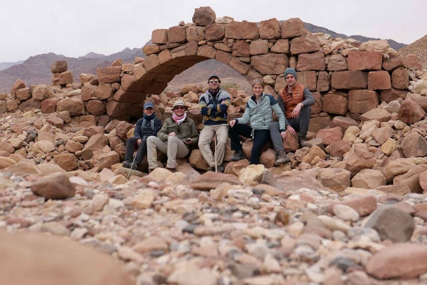 A group of people sitting under a stone archway in a rocky landscape. 1