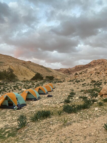 A row of tents set up on a rocky hillside under a cloudy sky. 2