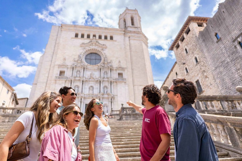 A group of people standing on steps in front of a historic building with a large circular window and a bell tower. 3