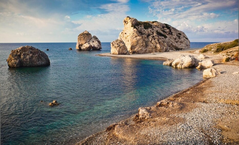 A coastal landscape with large boulders, clear blue water, and a pebbly beach. 5