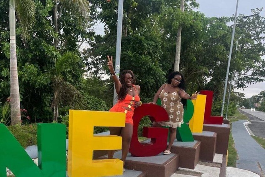 Two people sitting on steps with large colorful letters spelling 'NEGATIV' in the background. 1