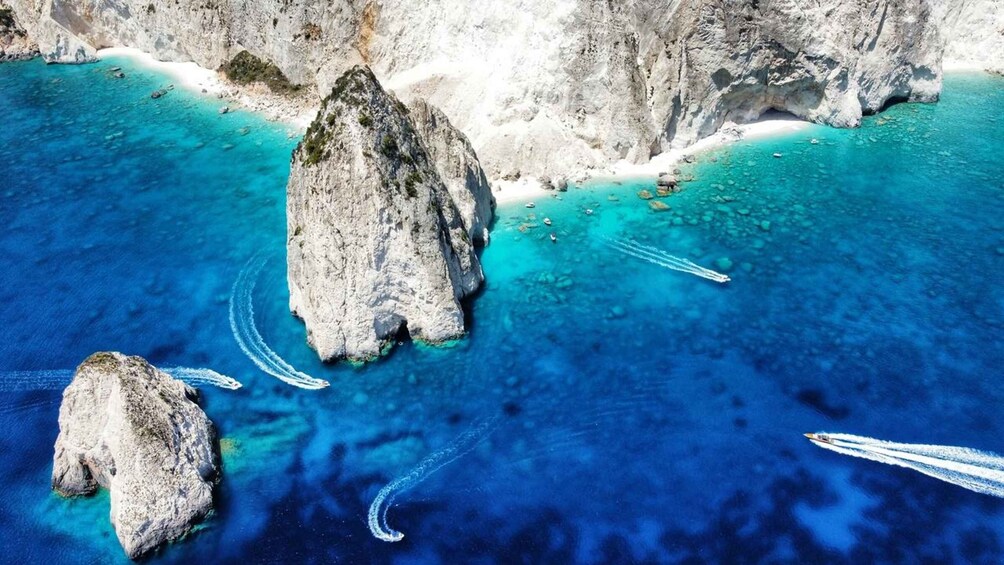 A coastal landscape with clear turquoise waters, rocky formations, and boat wakes. 2