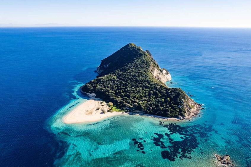 An aerial view of a small island with a central peak, surrounded by clear turquoise waters and a sandy beach. 3