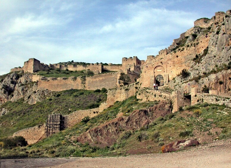 A historic stone fortress on a hillside with a large arched entrance and a small bridge. 3