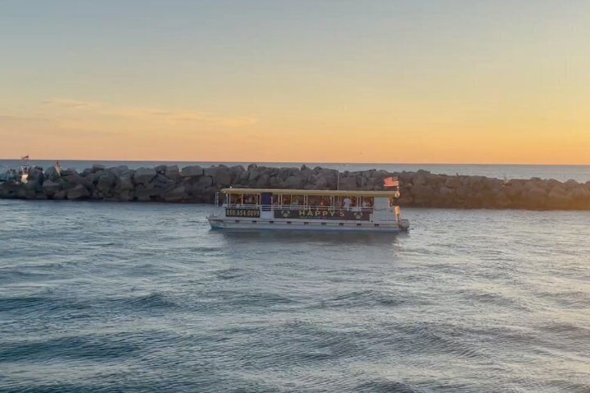 A boat with 'HAPPY S' on its side sailing on calm waters near a rocky breakwater during sunset. 2