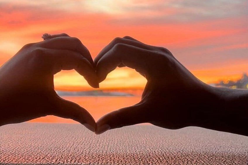 Dos manos formando una forma de corazón contra un cielo al atardecer. 3