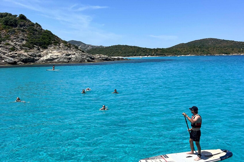 A person standing on a paddleboard in clear blue water with a mountainous landscape in the background. 5