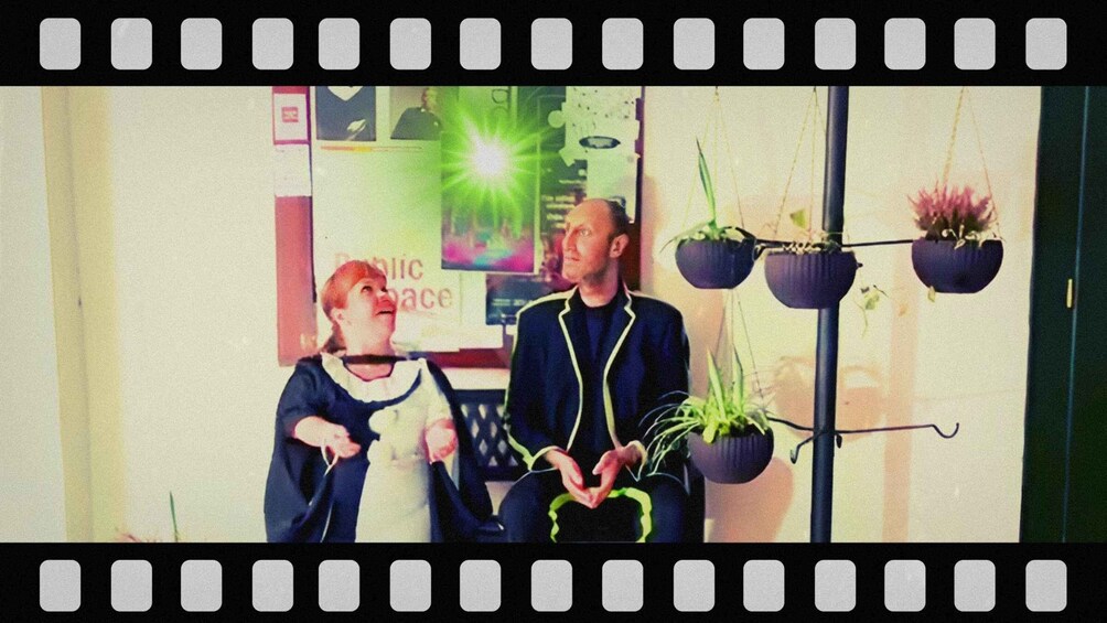 Two people in a room with a sign that reads 'Public Space' and hanging planters with plants. 3