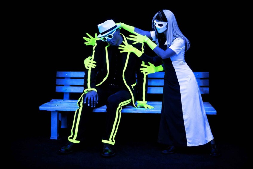 A person in a white dress and mask sitting on a bench with neon outlines. 1