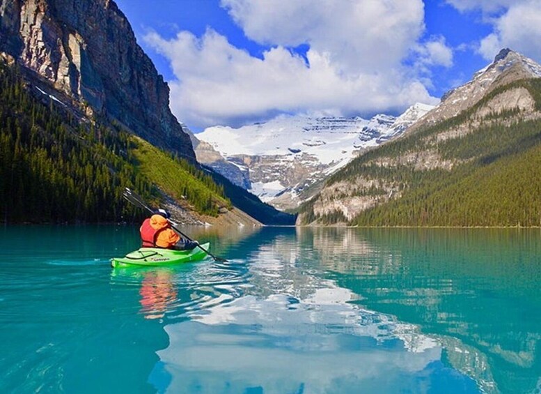 A kayaker on a turquoise lake surrounded by mountains and forests. 2