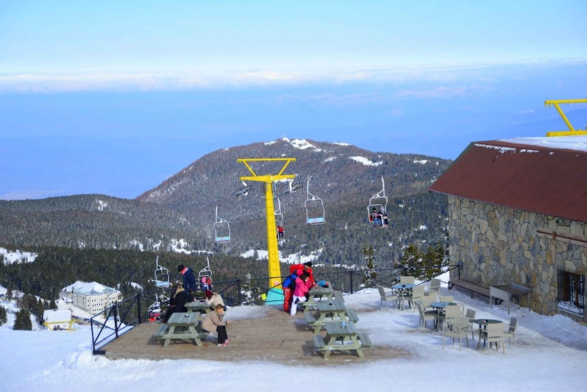 A snow-covered mountain with a ski lift, picnic tables, and a stone building. 2