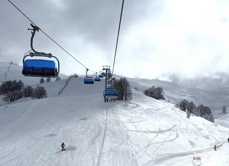 A ski lift with blue chairs ascending a snowy slope. 1