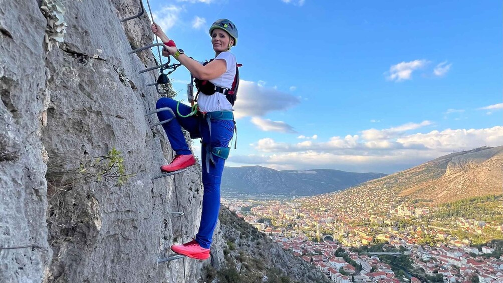 A person rock climbing a steep cliff with a cityscape in the background. 1