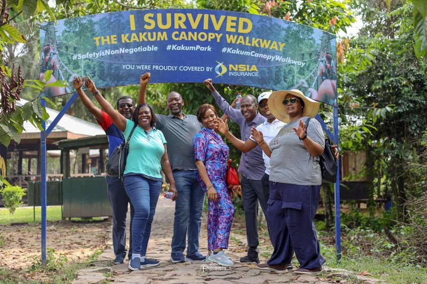 A group of people standing under a sign that reads 'I SURVIVED THE KAKUM CANOPY WALKWAY' with various hashtags and the NSIA Insurance logo. 3