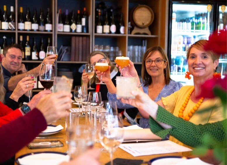 A group of people toasting with drinks at a bar with wine bottles in the background. 2