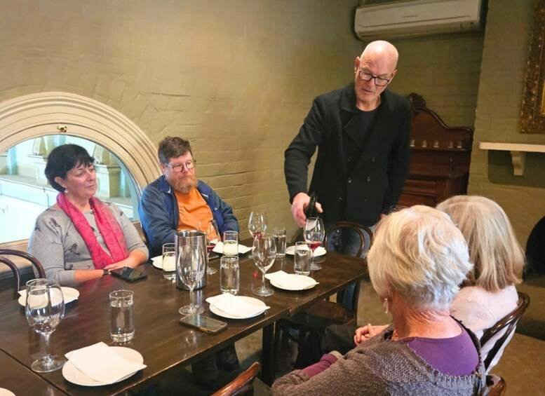 A group of people seated around a table with wine glasses and plates, in a room with a fireplace and a mirror. 4
