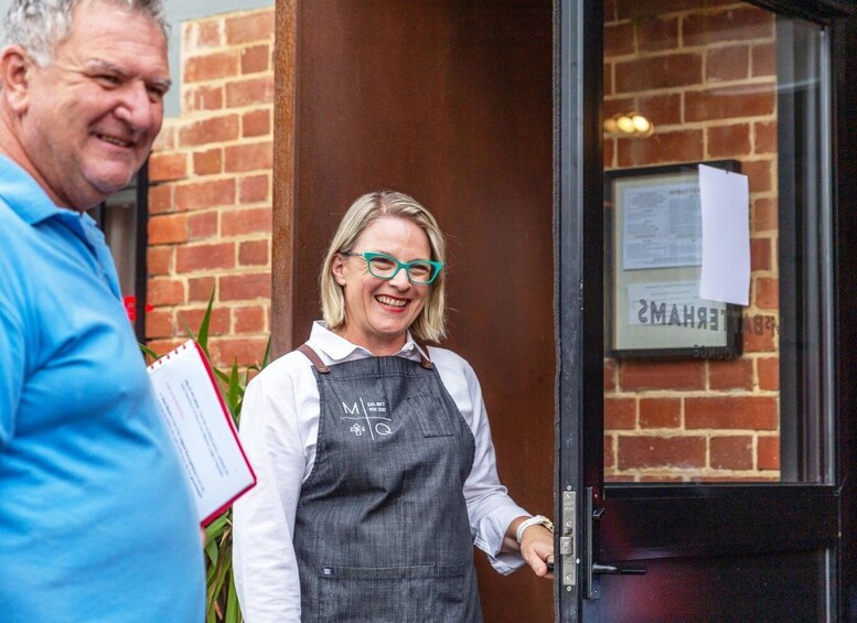 A person in a grey apron standing at a door with a sign that reads 'EMANZ.' 5