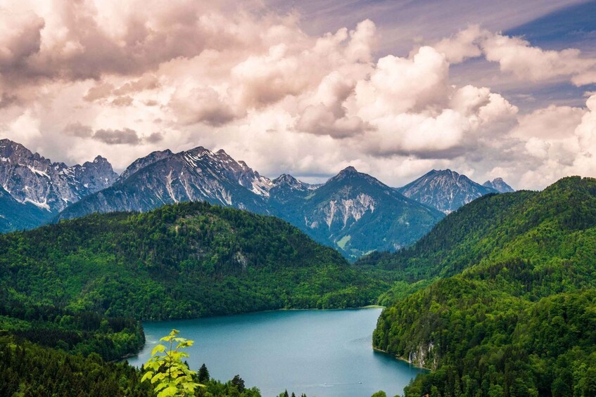 A mountainous landscape with a lake surrounded by dense forests and snow-capped peaks under a cloudy sky. 3