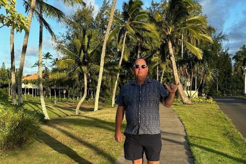 A man standing on a sidewalk with palm trees and a clear sky in the background. 3