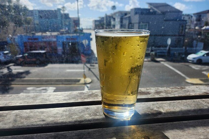 A glass of beer on a wooden ledge with a view of a street and buildings in the background. 5