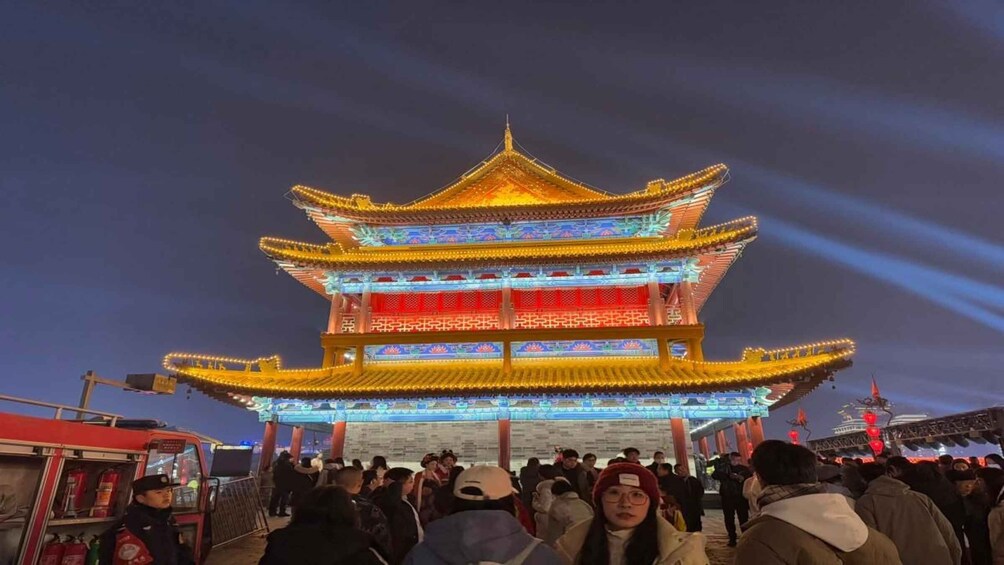 A traditional multi-tiered building with illuminated red and blue lights, surrounded by a crowd of people. 4