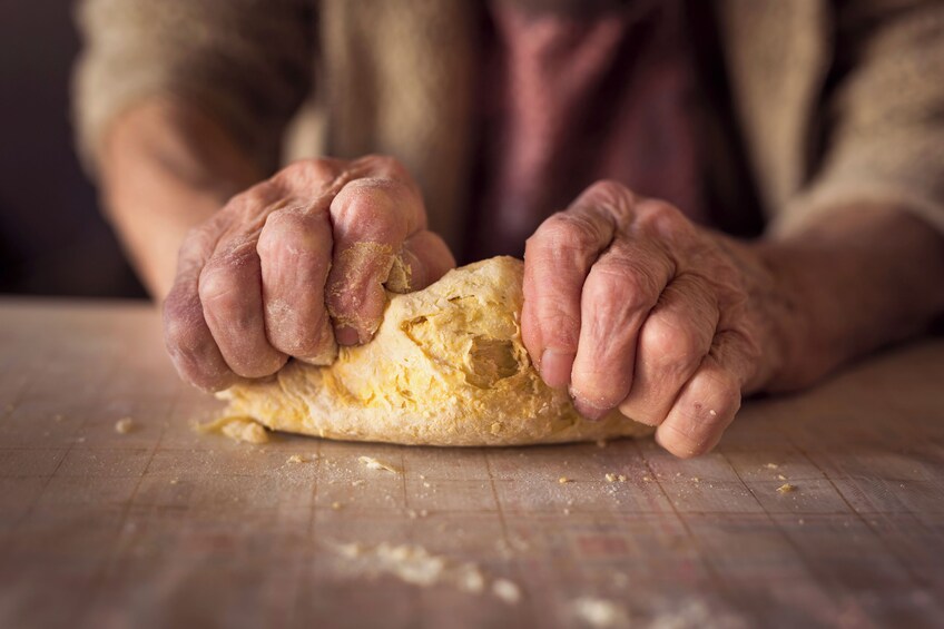 An elderly person kneading dough on a wooden surface. 2
