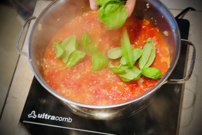 A pot of tomato sauce with basil leaves on a stovetop. 5