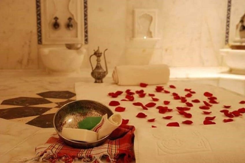 Une salle de bain avec une baignoire, un lavabo et un bol décoratif rempli de pétales de roses, posé sur le sol. 5