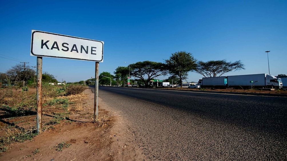 A road sign for 'KASANE' with a clear sky and a truck on the roadside. 1