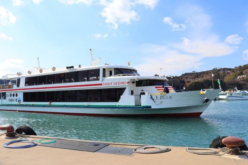 A large white ferry with 'SIGHT SEEING' written on the side, docked at a pier with calm water and a hilly landscape in the background. 3