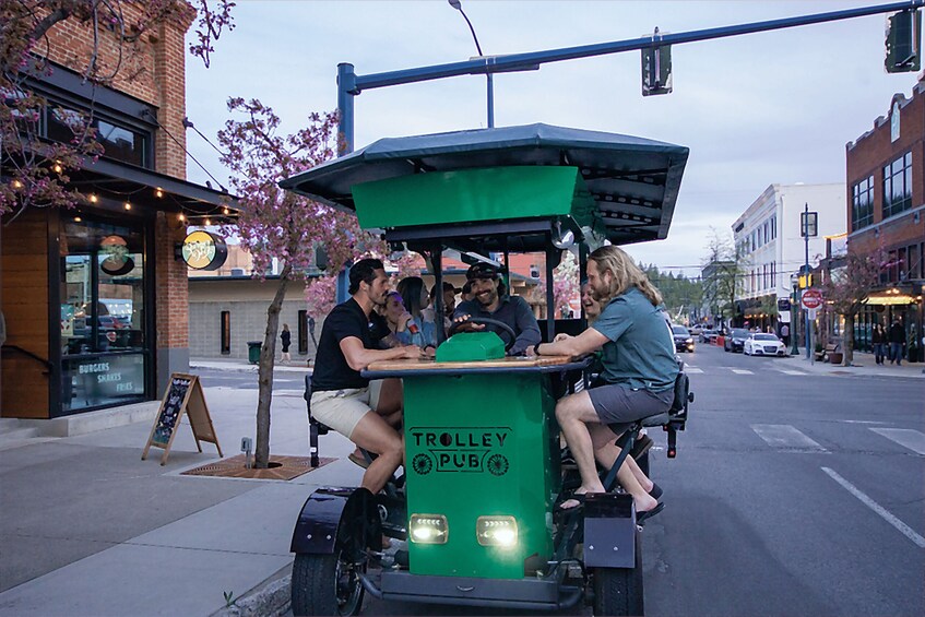 A green trolley with 'TROLLEY PUB' written on it, parked on a city street with buildings and cars in the background. 1