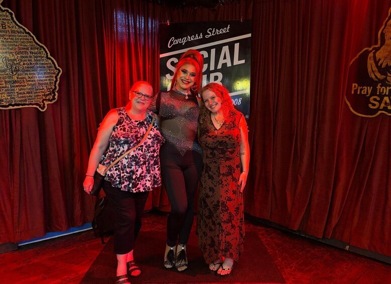 Three people standing in front of a red curtain backdrop with a sign that reads 'Congress Street.' 2