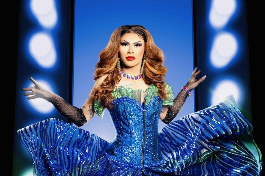 A person in a blue sequined dress with a green top and black fishnet sleeves. 1