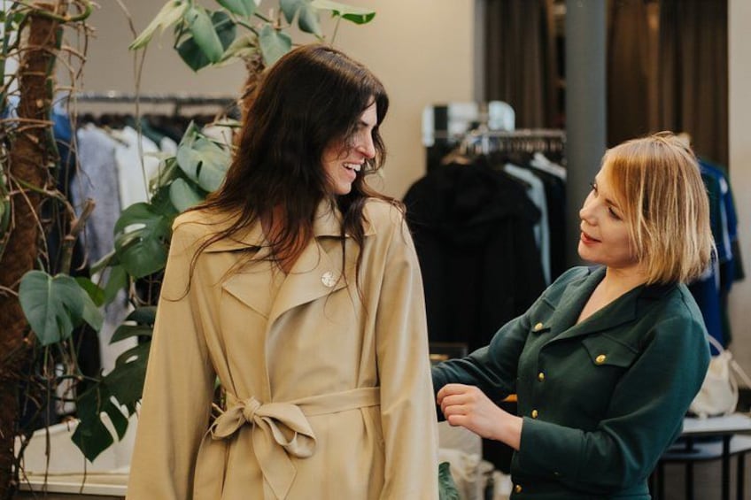 Two people in a clothing store, one adjusting a beige trench coat. 2