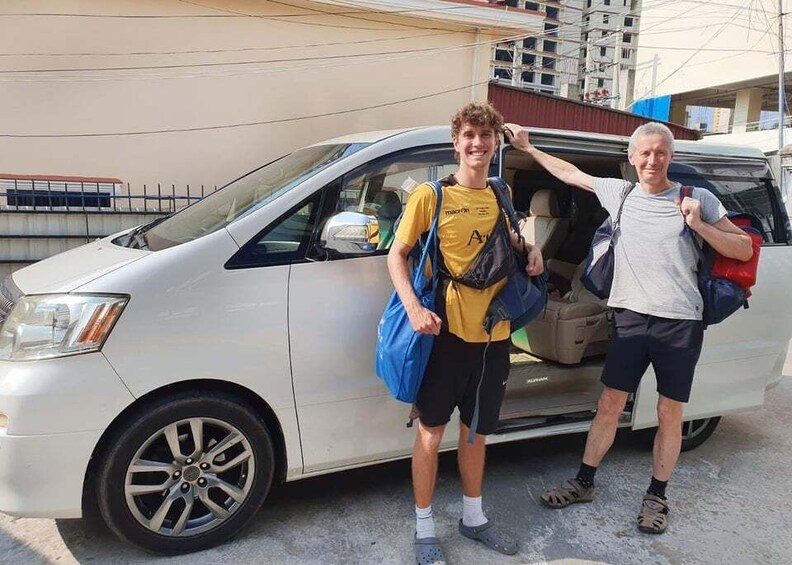 Two people standing next to a white van with luggage. 1