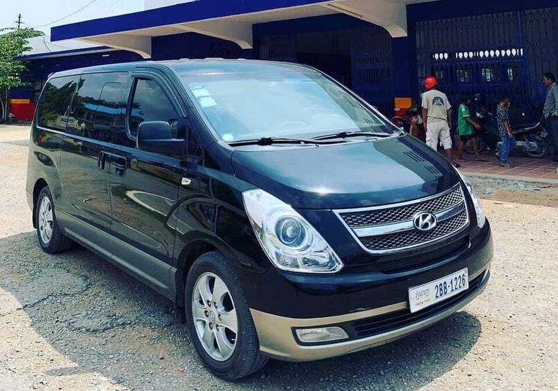 A black Hyundai minivan parked on a gravel surface with a blue building in the background. 3