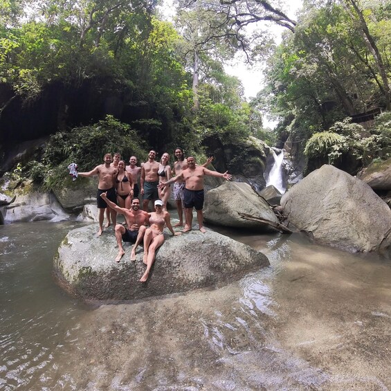 A group of people posing on rocks by a waterfall in a forested area. 1